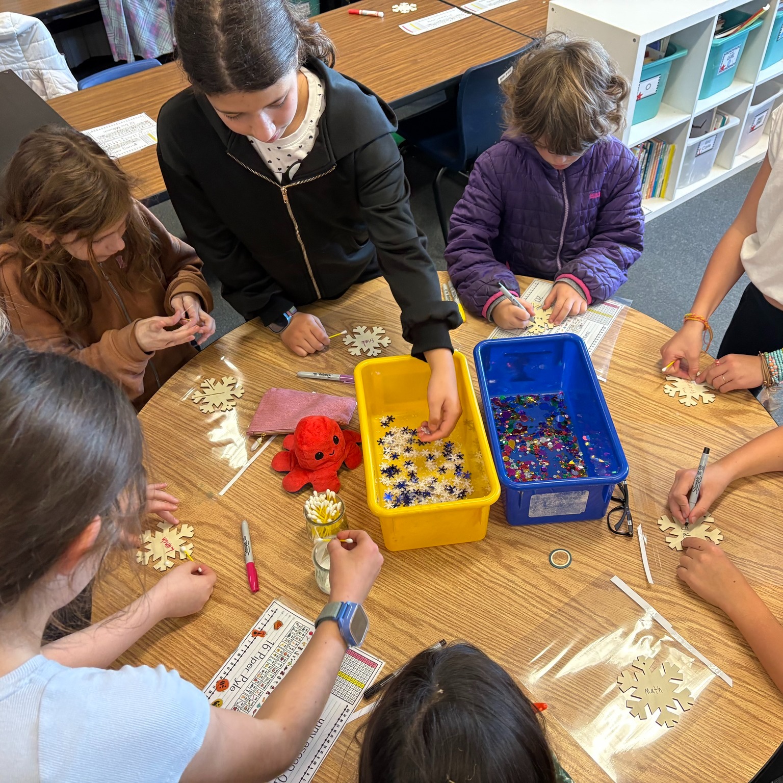 Children work at a table to decorate snowflakes at school.