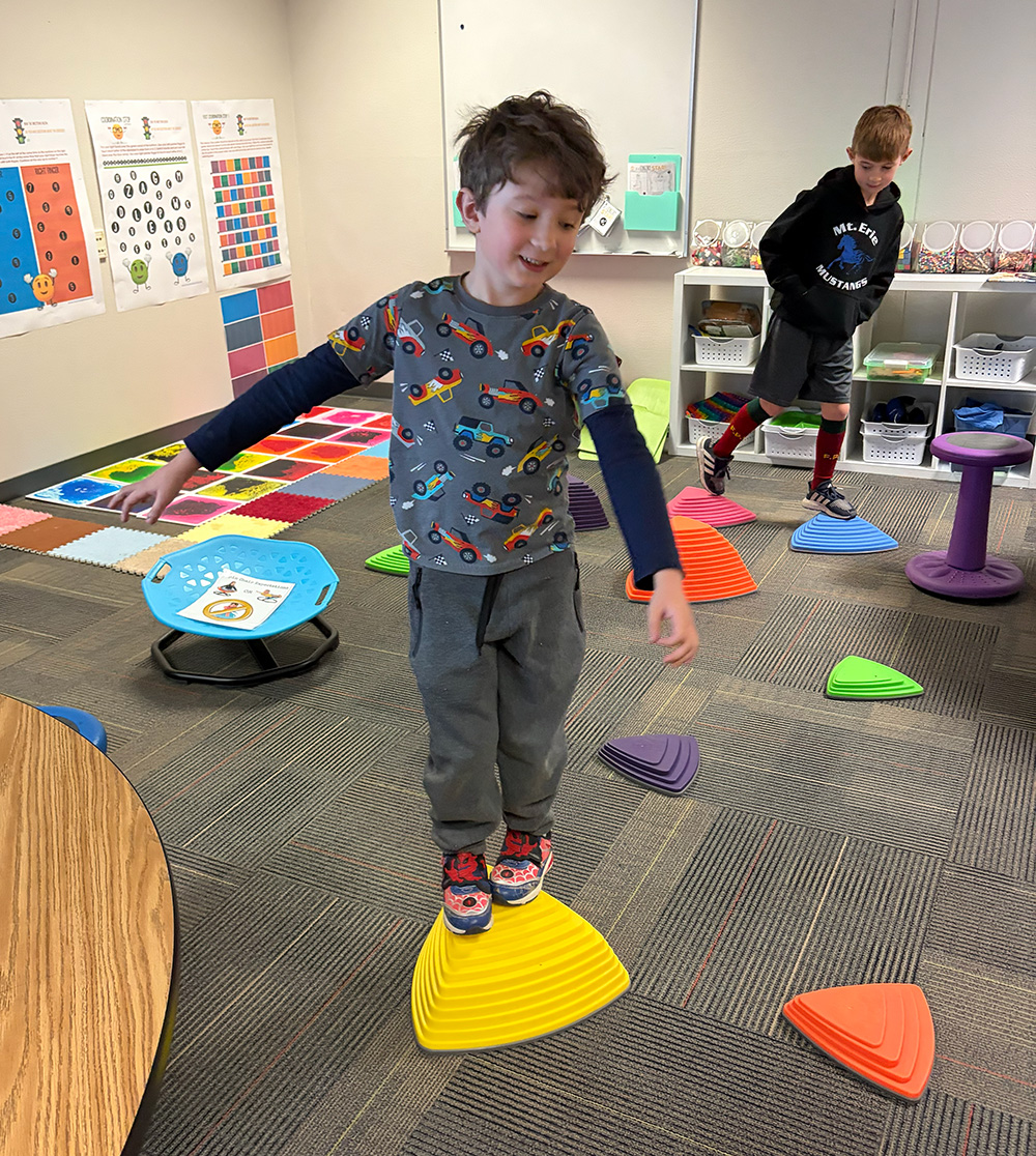 School Block Grant funding helped purchase sensory materials that support students' social-emotional learning. A student carefully balances on a yellow triangle as part of emotional regulation.