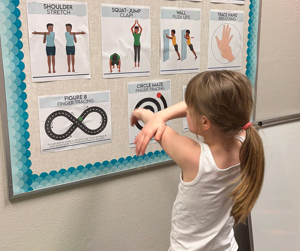 Students use sensory materials in a variety of ways—to regulate emotions, refocus their attention, and take meaningful breaks so they can return to learning ready to succeed. A student stretches in front of a poster in her classroom.