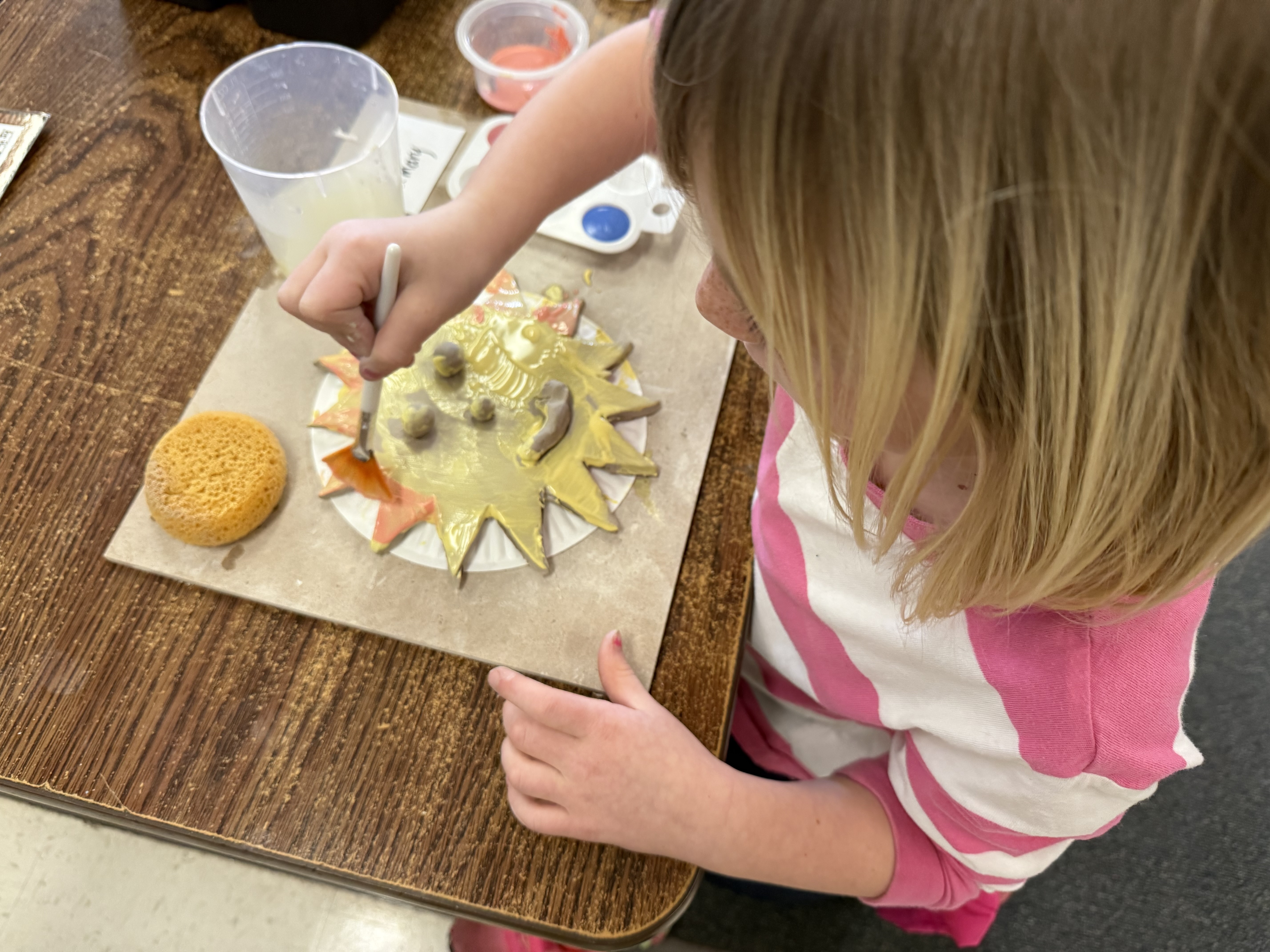 A child paints her clay creation yellow and orange..
