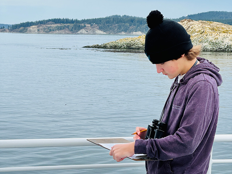 A student wearing a purple hoodie documents wildlife observations on a Salish Sea School trip aboard Island Adventures, sponsored by Anacortes Schools Foundation.